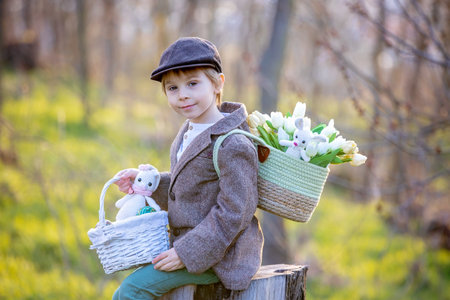 Beautiful stylish toddler child, boy, playing with Easter decoration in the park, springtime on sunsetの写真素材