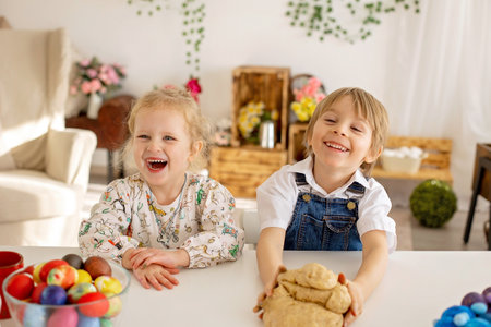 Little blond toddler boy child with sister, preparing dough for easter brioche buns, sweet easter bread with nuts and dry fruits at homeの写真素材