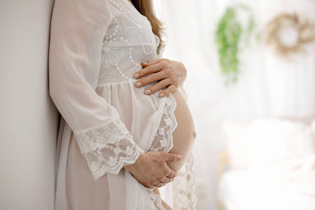 Portrait of young pregnant attractive woman, standing by the window, dressed in white dress, isolated imageの写真素材