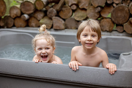 Children, boy and girl, playing in hydromassage bathtub, whirlpool in the backyard of the houseの写真素材