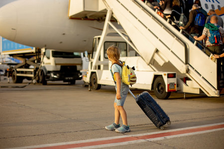 Cute blond child, kid with backpack, boarding airplane at the airport on sunset, enjoying the view...