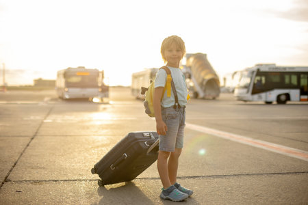 Cute blond child, kid with backpack, boarding airplane at the airport on sunset, enjoying the view from outsideの写真素材