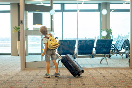 Cute blond child, kid with backpack, boarding airplane at the airport on sunset, enjoying the view from outsideの写真素材