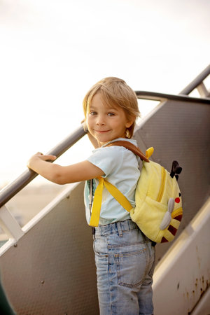 Cute blond child, kid with backpack, boarding airplane at the airport on sunset, enjoying the view from outsideの写真素材
