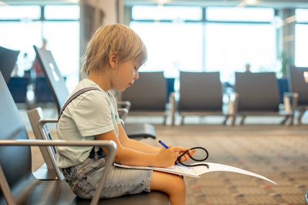 Child, cute boy, traveling with family, waiting at the airport to board the aircraft, drawing picture in the waiting hallの写真素材