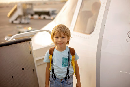 Cute blond child, kid with backpack, boarding airplane at the airport on sunset, enjoying the view from outsideの写真素材