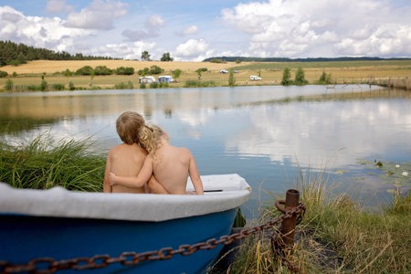 Beautiful blond children, boy and girl, siblings, sitting on a boat in a lake, enjoying amazing summer atmosphere togetherの写真素材