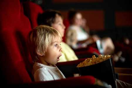 Cute child, boy, watching movie in a cinema, eating popcorn and enjoying the filmの写真素材