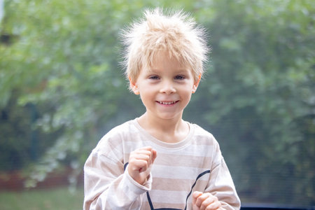 Cute little boy with static electricy hair, having his funny portrait taken outdoors on a trampolineの写真素材