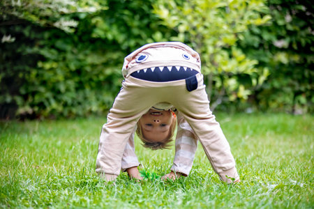 Little preschool child, with funny cloths, making smile face, looking upside down between his legs in gardenの写真素材