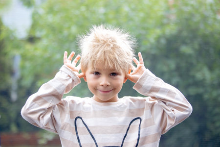 Cute little boy with static electricy hair, having his funny portrait taken outdoors on a trampolineの写真素材