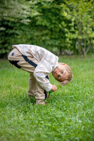 Little preschool child, with funny cloths, making smile face, looking upside down between his legs in gardenの写真素材