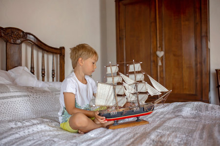 Cute blond child, boy, playing at home with toys, ship, dolls, autentic houseの写真素材