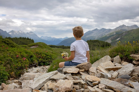 Beautiful blond child, boy, gathering wild flowers fom mother in the mountains in Switzerland, summertimeの写真素材