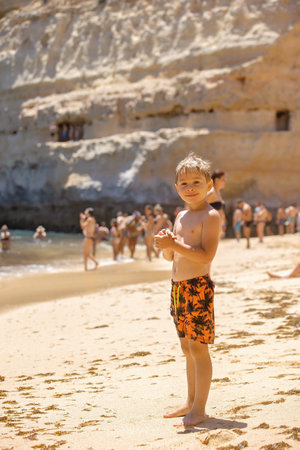 Child, tickling sibling on the beach on the feet with feather, kid cover in sand, smiling, laughing, enjoying some funの写真素材
