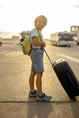 Cute blond child, kid with backpack, boarding airplane at the airport on sunset, enjoying the view from outsideの写真素材
