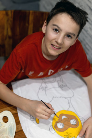 Child, making creative art picture on a t-shirt, drawing it himself and painting it with textile...