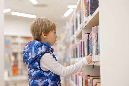 Smart child, school boy, educating himself in a library, borrowing books to read