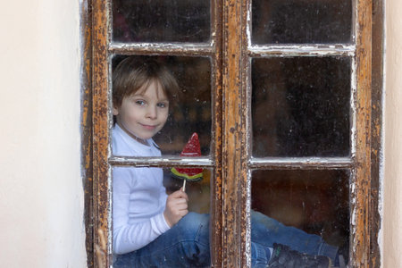 Cute child and maltese pet dog, sitting on the window and eating watermelon lollipop, smiling with...