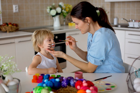Mother painting on little blond toddler boys' face easter bunny at home