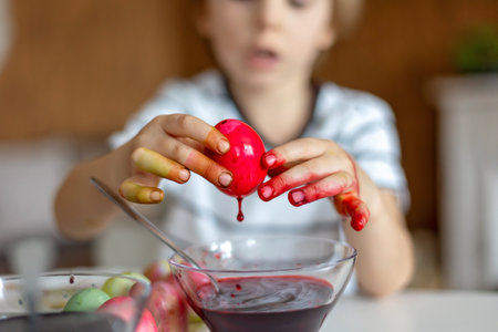 Beatiful blond child, boy, coloring and painting eggs for Easter at home, preparing for the holidays