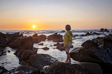 Happy children, enjoying sunset over the ocean with their family, rocky beach in Portugalの写真素材