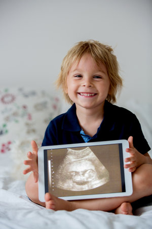 Cute toddler child, holding a picture of his little unborn baby sister from the ultrasound