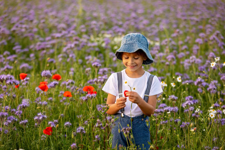 Beautiful school child in a flower field on sunset, playing with airlane and vintage suitcase, springtimeの写真素材