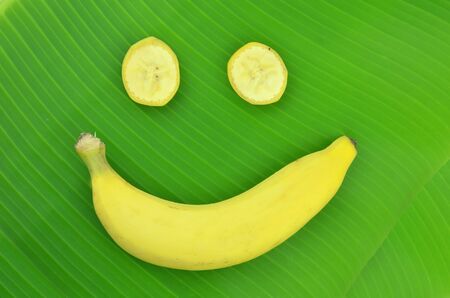 Yellow banana is placed on a green banana leaf in the shape of a smile.の写真素材