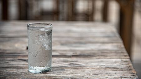 Glass of water placed on a wooden table, selective focus, blur some part.