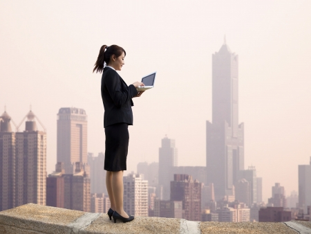 Businesswoman using computer and  stand on the top of a skyscraper with cityscape の写真素材