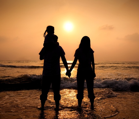 The silhouette of loving asian family walking while holding hands on beach at sunsetの写真素材