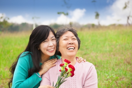 Smiling daughter and her mother with carnation flower on the grass fieldの写真素材