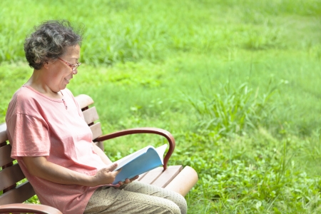 happy senior woman sitting on  bench and reading a bookの写真素材