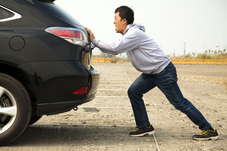Man pushing a broken car down the rock road 
