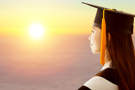 pretty female graduation is thinking future with sunset backgroundの写真素材