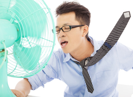 Young man cooling face under wind of fanの写真素材