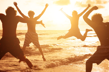group of young people jumping at the beach with sunset backgroundの写真素材