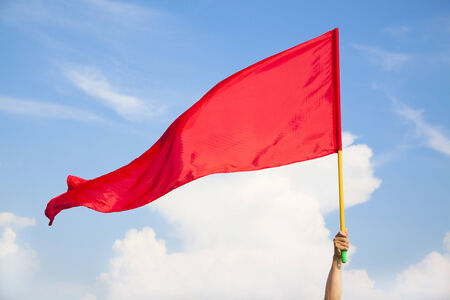 Hand waving a red flag with blue sky background の写真素材