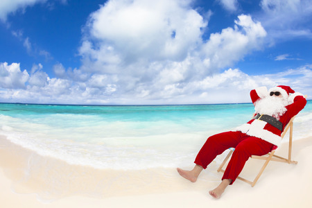 Santa Claus sitting on beach chairs with blue sky and cloud. Christmas holiday concept.の写真素材