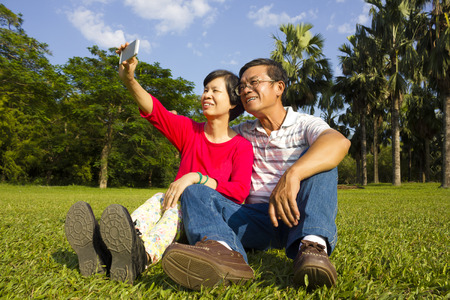 Asian Senior couple sitting on grassland and  taking picture by themselves outside