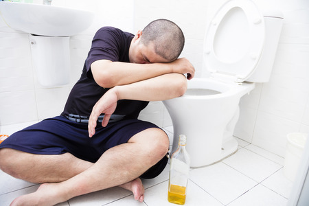 Drunk fat man with wine bottle in toiletの写真素材