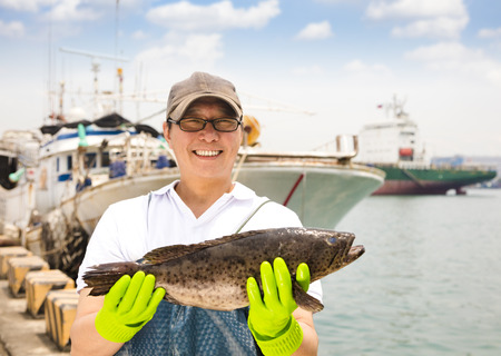 happy fisherman showing  fish before fishing shipの写真素材