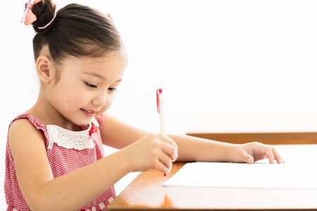 happy little girl writing at desk in classroomの写真素材