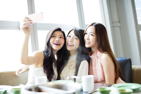 happy young girl friend taking selfie together in restaurantの写真素材