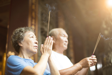 senior couple praying buddha with incense stick at templeの写真素材
