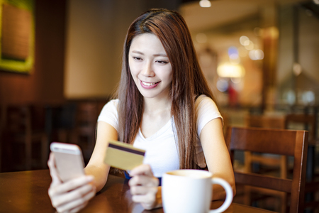 woman holding credit card and smart phone in coffee shopの写真素材