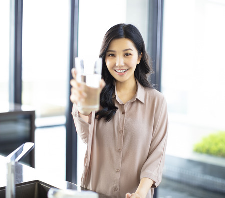 young woman showing drinking glass with water in kitchenの写真素材