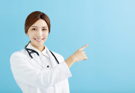 Smiling female doctor pointing with finger on blue backgroundの写真素材