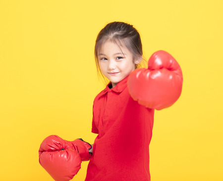 happy little girl with red boxing gloves on yellow backgroundの写真素材